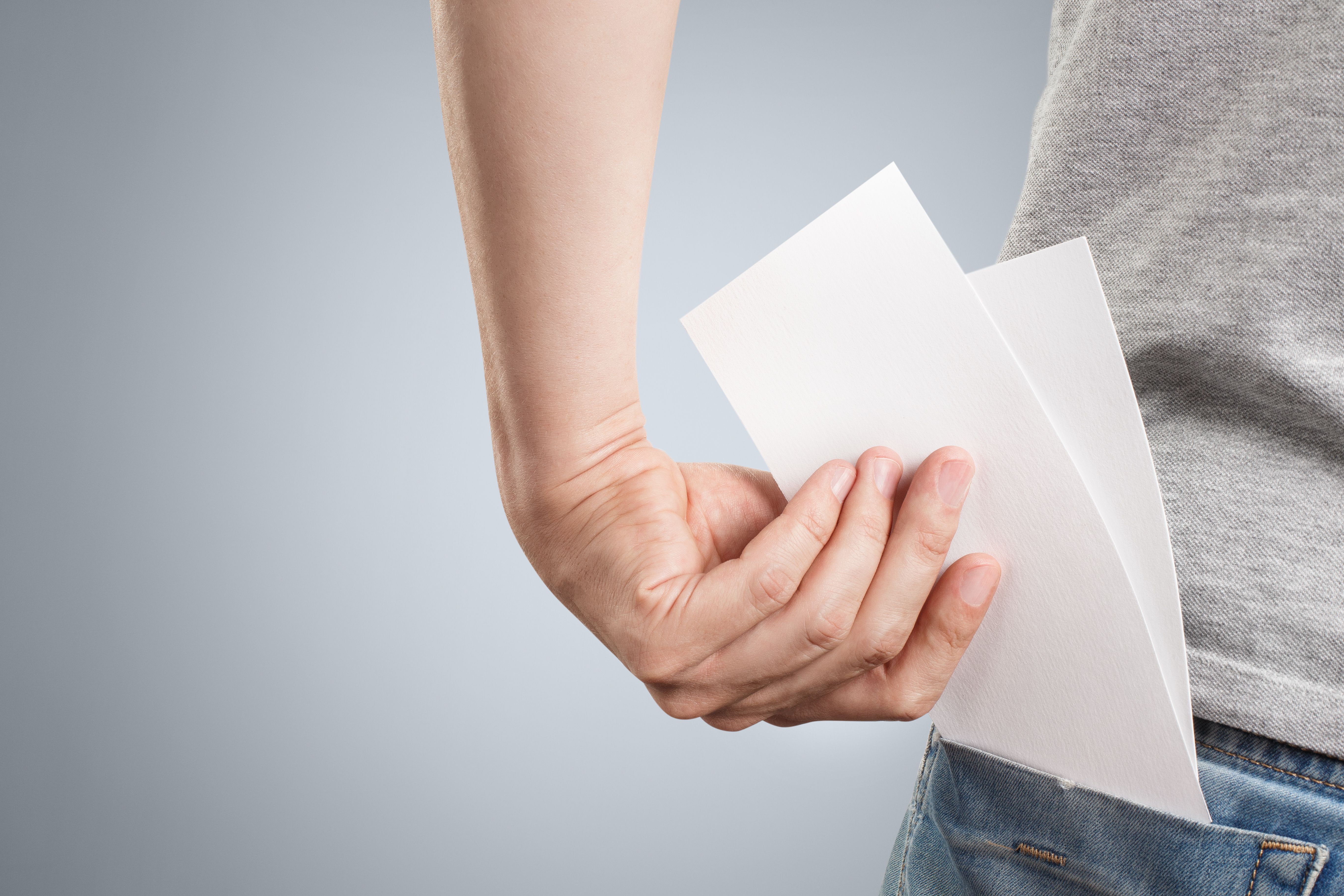 Hand putting two sheets of paper into the back pocket on gray background