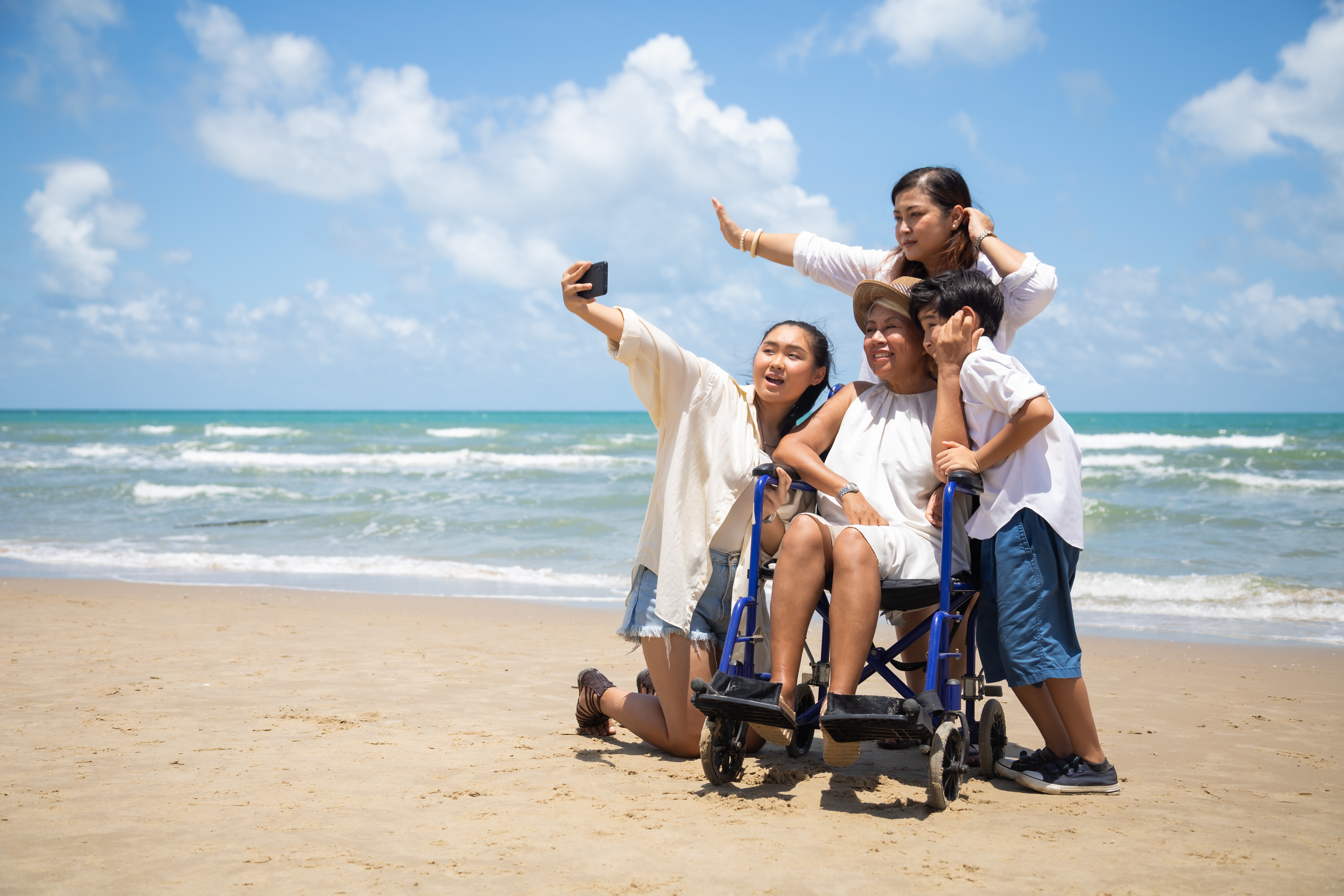 Happy family and woman elderly handicap on wheelchair making salfie together on the beach.